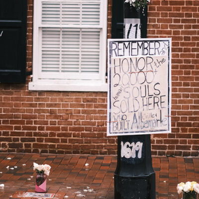 White poster that says Remember and honor the 2,000 human souls sold here who built C’ville and Albemarle.