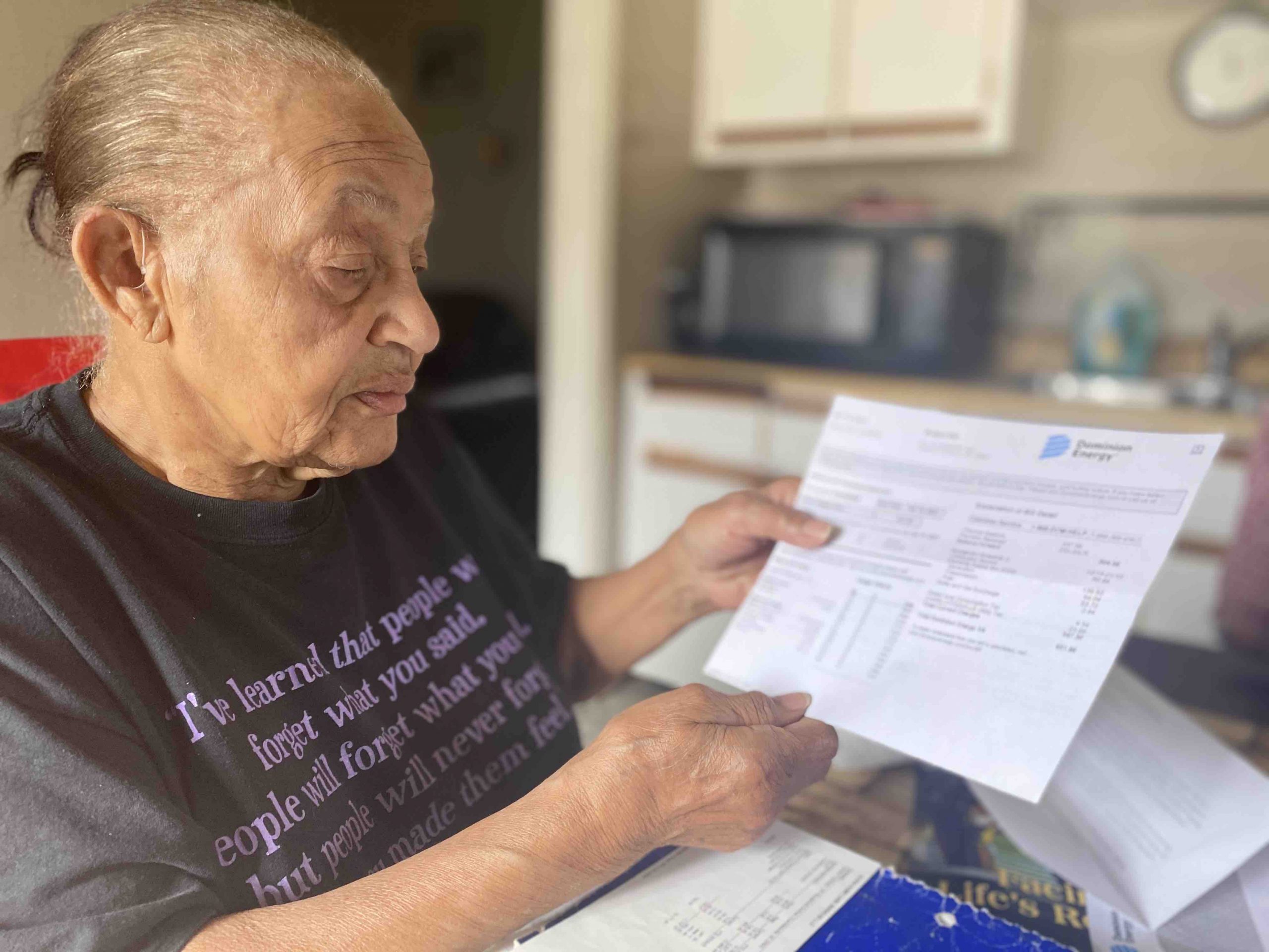 Carolyn Johnson stands in her kitchen showing her Dominion energy bill