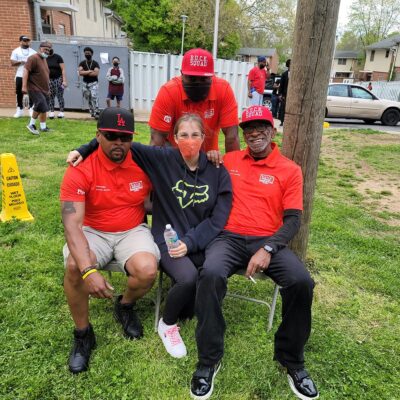 Three members of the BUCK squad sit with an event attendee during a community day at Westhave public housing community