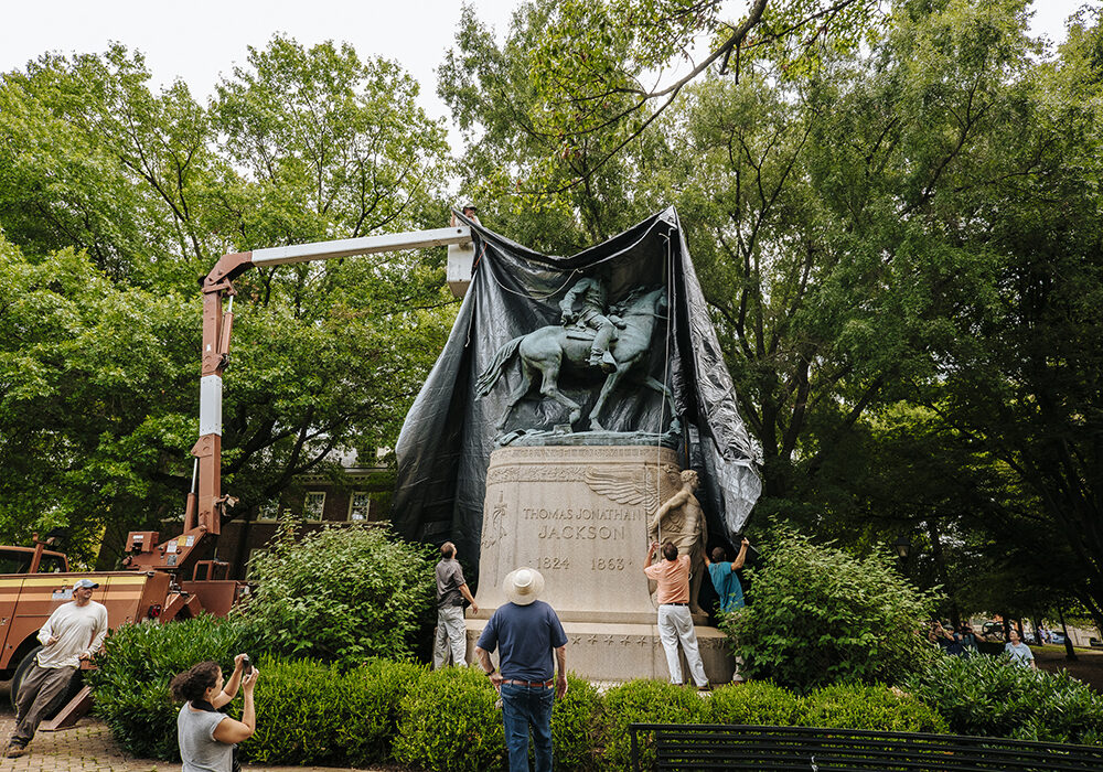 A crane puts a black shroud over Charlottesville's Jackson statue while seven people watch