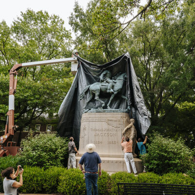 A crane puts a black shroud over Charlottesville's Jackson statue while seven people watch