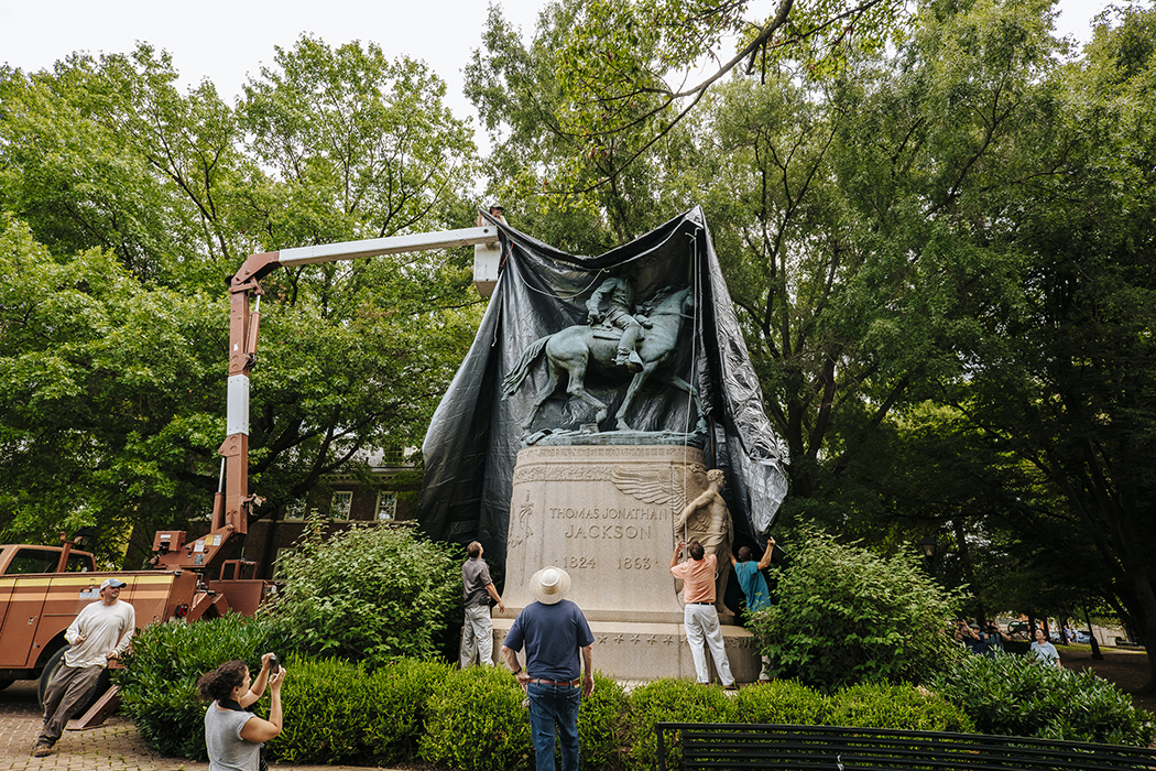 A crane puts a black shroud over Charlottesville's Jackson statue while seven people watch