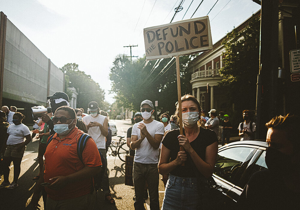 Group of protestors in downtown Charlottesville, one person holds a Defund the Police sign